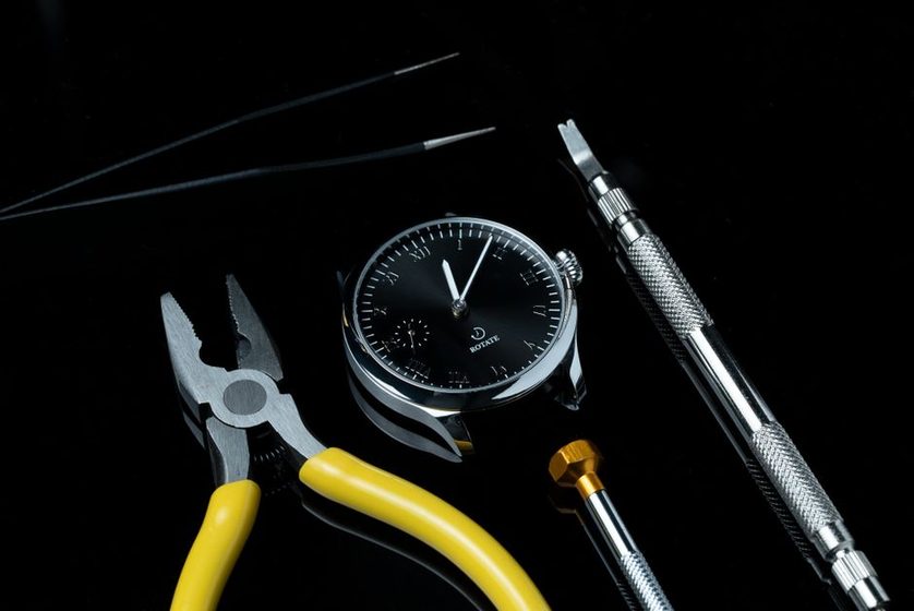A watchmaker's hands adjusting a balance wheel under a loupe