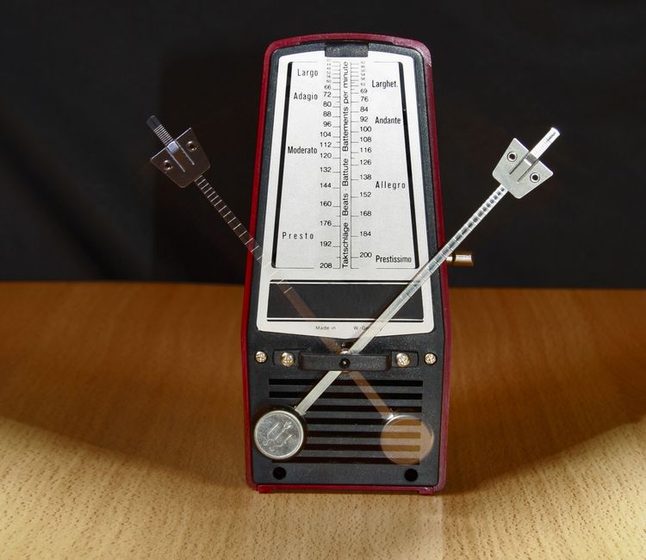 A mechanical metronome sitting next to a wristwatch on a table