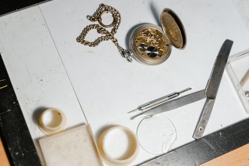 A disassembled mechanical watch movement laid out on a cloth mat with brass tools nearby